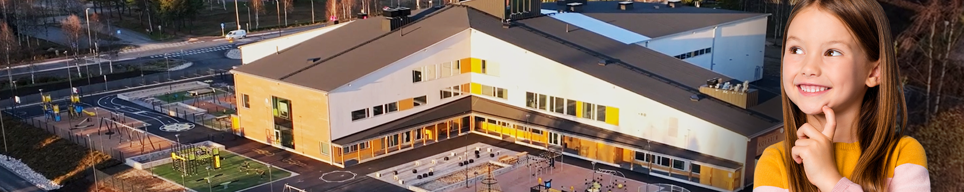 Kuvassa on suuri, moderni koulurakennus, jonka edessä on leikkikenttä ja urheilukenttä. Rakennuksen ympärillä on metsää ja taustalla näkyy laaja metsämaisema. Kuvan etualalla on lapsi, joka hymyilee ja katsoo ylöspäin mietteliäänä.